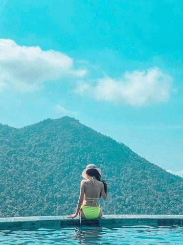 a woman sitting in the water with a hill in the background at Mimosa 226 - phòng săn mây in Tam Ðảo
