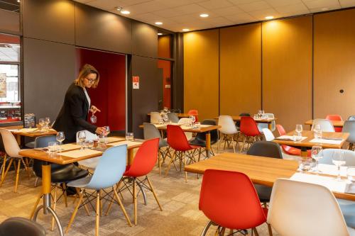 a woman standing in a restaurant with tables and chairs at ibis Le Puy-en-Velay Centre in Le Puy en Velay