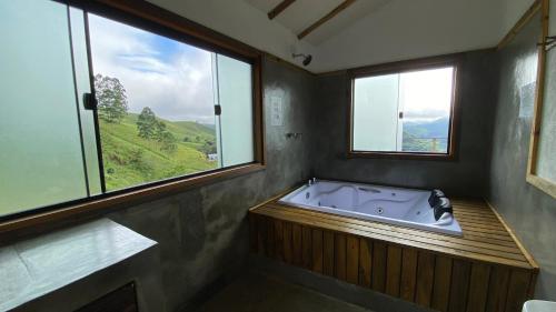 a bath tub in a bathroom with two windows at Pousada Verde Serena SFX in São Francisco Xavier