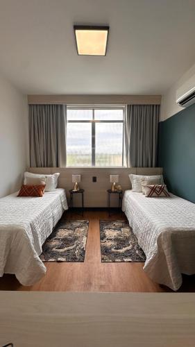 a bedroom with two beds and a window and a rug at Seu Refúgio Apartamento moderno e aconchegante no Centro de Juiz de Fora in Juiz de Fora