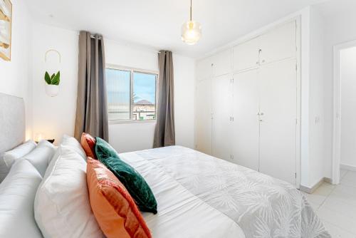 a white bedroom with a bed with pillows and a window at Lolas in Puerto del Carmen