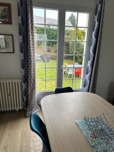 une table et des chaises dans une pièce avec une grande fenêtre dans l'établissement Le Temps de Vivre - Maison avec jardin proche Deauville, à Touques