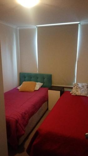 two beds in a small room with red sheets at Departamento amplio en Los Ángeles, Chile in Los Ángeles