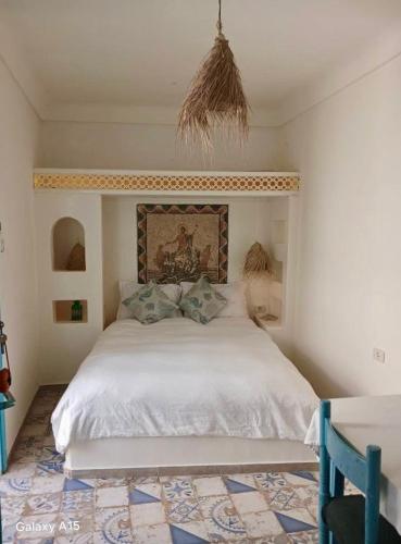 a bedroom with a white bed with a painting on the wall at Dar Evelyne by Daldoul in Mahdia