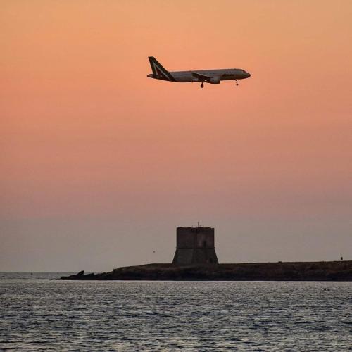 a plane flying over the water with a lighthouse in the background at Da Turiddu in Cinisi