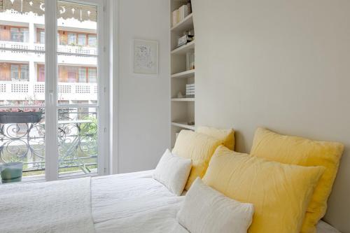 - un lit blanc avec des oreillers jaunes dans une chambre dotée d'une fenêtre dans l'établissement Elegant 1-Bedroom Apartment, à Paris
