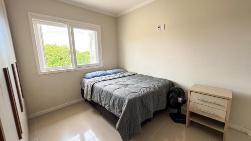a small bedroom with a bed and a window at Casa 3 min da praia 2 suítes churrasqueira garagem in Tramandaí