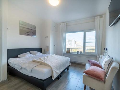 a bedroom with a bed and a chair and a window at Apartment by North Sea with Stunning Views in Middelkerke