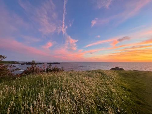 a sunset over the ocean with a field of grass at SADO Cottage SUNSETHILLS in Sado