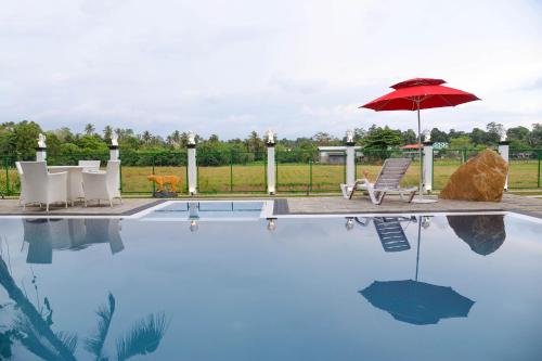 a pool with a red umbrella and chairs and a table with an umbrella at The Jungle Dream World in Wadduwa