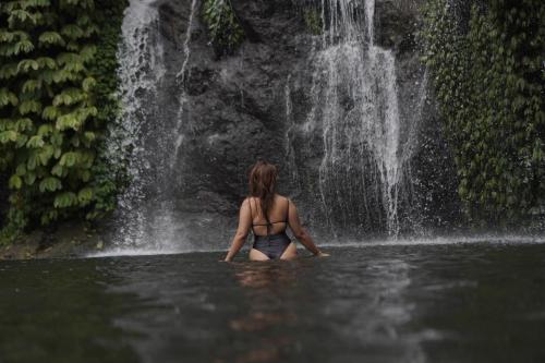 a woman sitting in the water in front of a waterfall at Maha Hills Resort by Mahaprana Experience in Lovina