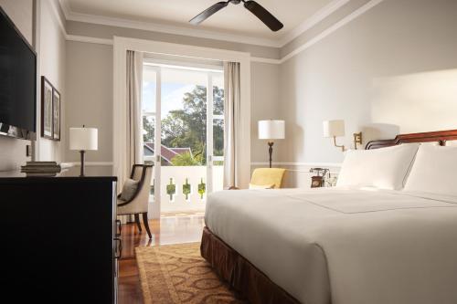 a white bedroom with a bed and a window at Raffles Grand Hotel d'Angkor in Siem Reap