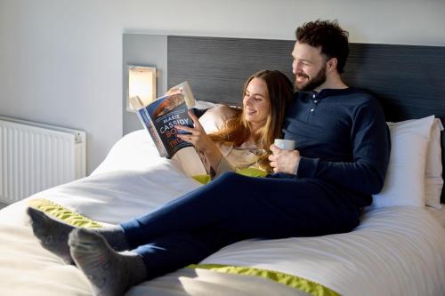 a man and a woman sitting on a bed reading at Newtown Park Hotel in Wexford