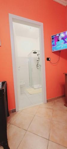 a bathroom with an orange wall with a shower and a television at B&B JOY in Nettuno