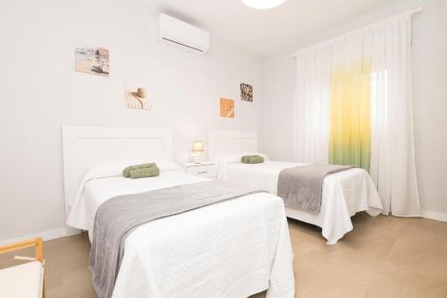 a white room with two beds and a window at Las Camelias in Chiclana de la Frontera