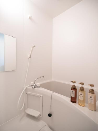 大阪市にある川House今里の3本のボトルが置かれたバスタブを備えた白いバスルーム
