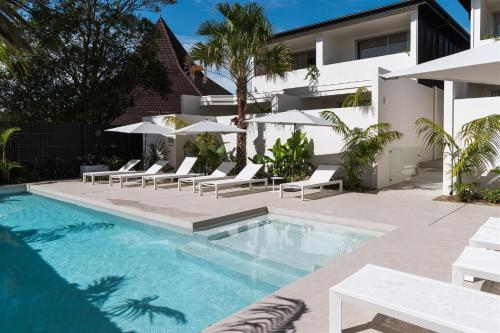 Una piscina con sillas y sombrillas al lado de un edificio. en The Hide Byron Bay, en Byron Bay
