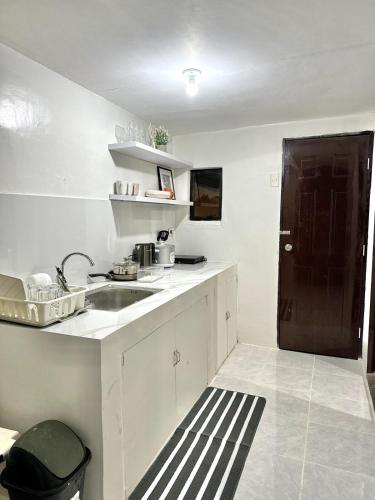 a white kitchen with a sink and a black door at Cozy 3BR Bungalow House with Netflix & Games in Davao City