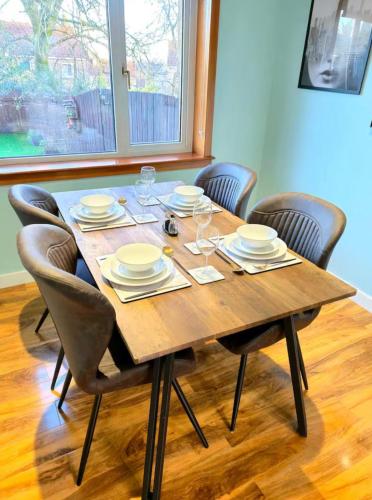 a wooden table with chairs and plates and wine glasses at Super luxury 2 bedroom, full house sleep 5 with garden & parking close to airport in Elderslie