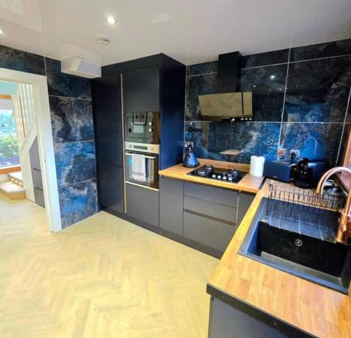 a kitchen with black and blue tiled walls at Super luxury 2 bedroom, full house sleep 5 with garden & parking close to airport in Elderslie