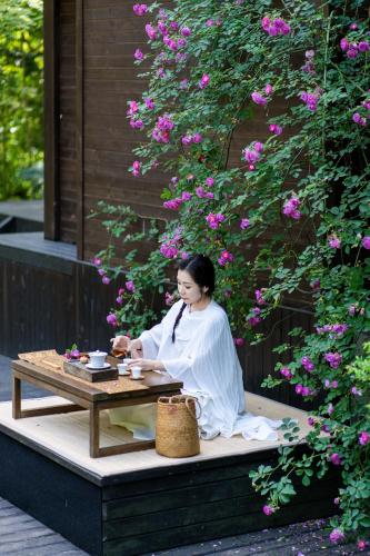 a woman sitting on a bench next to a table at 青城山坐忘森林疗愈酒店 in Dujiangyan