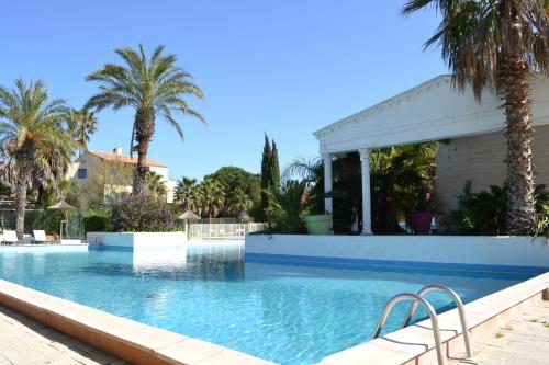 a swimming pool with palm trees and a house at Malibu Village in Canet-en-Roussillon