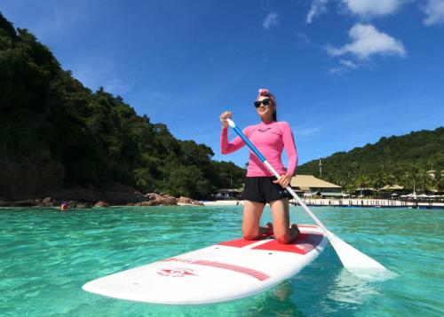 a woman is standing on a paddle board in the water at The Taaras Beach & Spa Resort in Redang Island