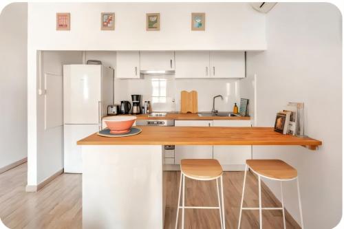 une cuisine avec des placards blancs et un comptoir avec deux tabourets dans l'établissement L'appartement de la Roquette centre historique Arles, à Arles