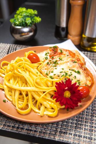 a plate of pasta with meat and a flower on a table at Hotel Darolt Criciúma in Criciúma