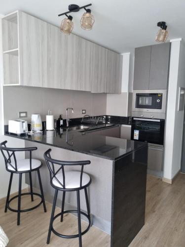 a kitchen with two bar stools and a black counter top at Dpto Nuevo Miraflores in Santiago