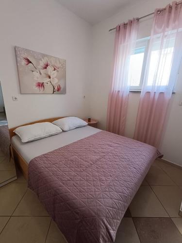 a bedroom with a bed and a window with pink curtains at Apartments Kraljić in Baška