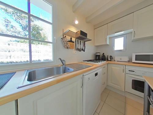 une cuisine avec des armoires blanches, un évier et une fenêtre dans l'établissement Charmante maison à 250m de la plage avec jardin, terrasse ensoleillée et garage à vélo, L'Épine - FR-1-224B-161, à LʼÉpine