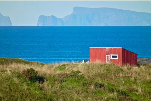 a red shed sitting on top of a hill next to the ocean at Helligvær Kystopplevelser AS in Bodø