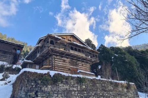 a log cabin in the snow with a stone wall at ArtVillage Naggar - Entire Katkuni Villa in Nagar
