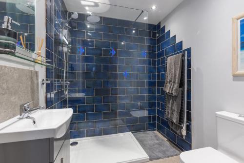 Un baño con azulejos azules, lavabo e inodoro. en Rockpool - Bude, en Bude
