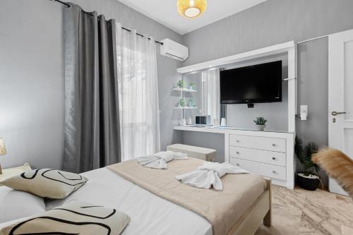 a white bedroom with two beds and a flat screen tv at Andy’s apartments in Georgioupolis