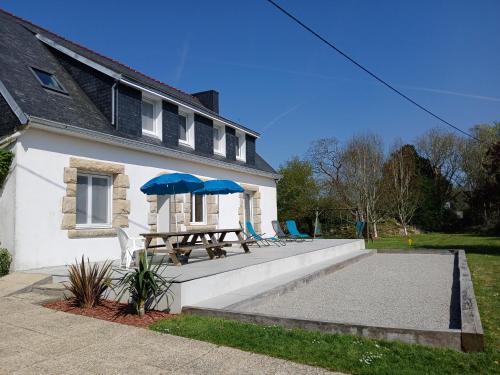 a house with a picnic table and two blue umbrellas at Gite de Pellein in Quéménéven
