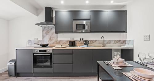 a kitchen with black appliances and a table with wine glasses at 1BR Apartment with Sofa Bed I Prime Town Centre Location I Gold St D-Lux, Modern Amenities, Walk to Train, Bus Stations, Shops & Cafés I Leisure and Business Stays Welcome MULTIPLE UNITS AVAILABLE in Northampton