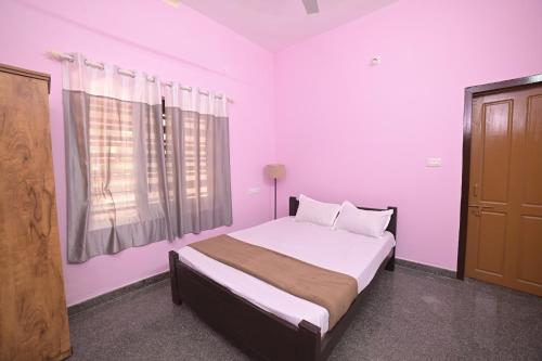 a bedroom with a bed with pink walls and a window at The Camp Club Beach Villa in Payyannūr