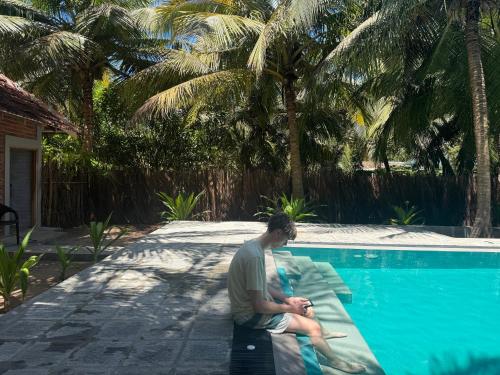 a man sitting on a bench next to a swimming pool at Agro Village Resort , Kalpitiya in Kalpitiya