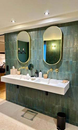 La salle de bains est pourvue de 2 lavabos et de 2 miroirs sur le mur. dans l'établissement FÓLKLORE Boutique Hôtel, à Sancerre