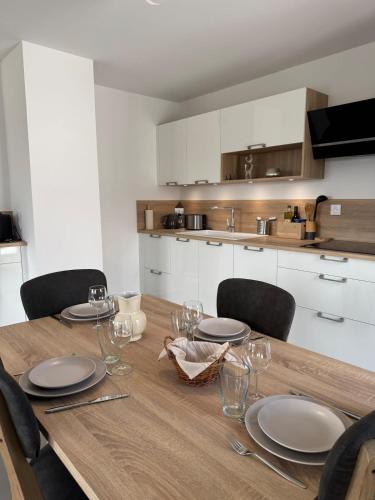 - une table en bois avec des assiettes et des verres dans la cuisine dans l'établissement Le Doublaix - Superbe T3 neuf - Parking privé -, à Aix-les-Bains