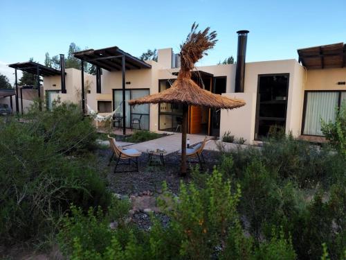 una casa con sombrilla de paja, sillas y mesa en Posada Los Chañares, en Ciudad Lujan de Cuyo