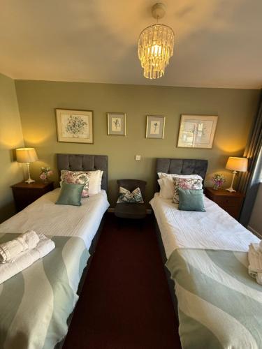 two twin beds in a room with a chandelier at Broadlands in Bourton on the Water