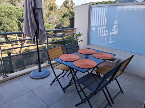une table et des chaises sur un balcon avec un parasol dans l'établissement Aux rivages de Sylvie - 150 m de la plage, à Calvi