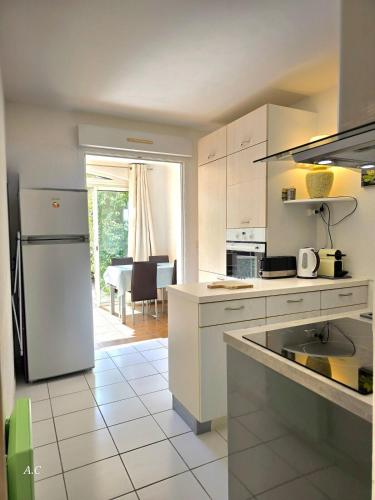 une cuisine avec des armoires blanches et un réfrigérateur blanc dans l'établissement Le Murier - Rez de jardin avec véranda, terrasse à 5min a pied de la mer avec parking - BY AURAconciergerie, aux Lecques