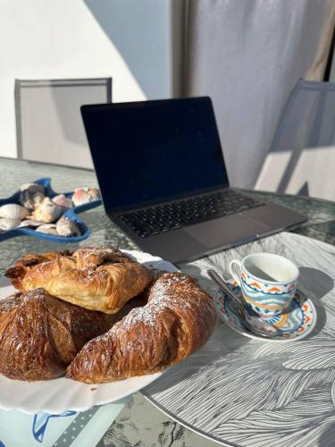 a table with a laptop and croissants and a plate of bread at Le Terrazze della Dolce Casa - Blue Wave - Casa Vacanza a Marina di Ragusa in Marina di Ragusa