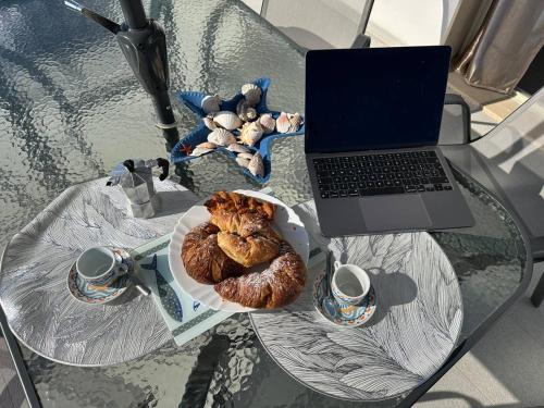 a glass table with a laptop and a plate of pastries at Le Terrazze della Dolce Casa - Blue Wave - Casa Vacanza a Marina di Ragusa in Marina di Ragusa