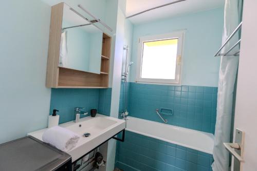 La salle de bains est pourvue de carrelage bleu, d'un lavabo et d'une fenêtre. dans l'établissement Très bel appartement Mulhouse Parking gratuit, à Mulhouse