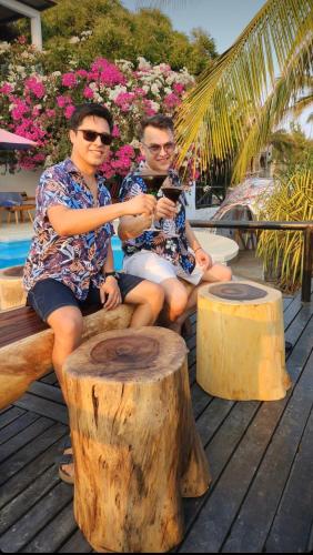 two men sitting on a wooden bench next to a tree stump at Beachfront Paradise Boutique Hotel - Breeze Room ll in Playa Agua Blanca
